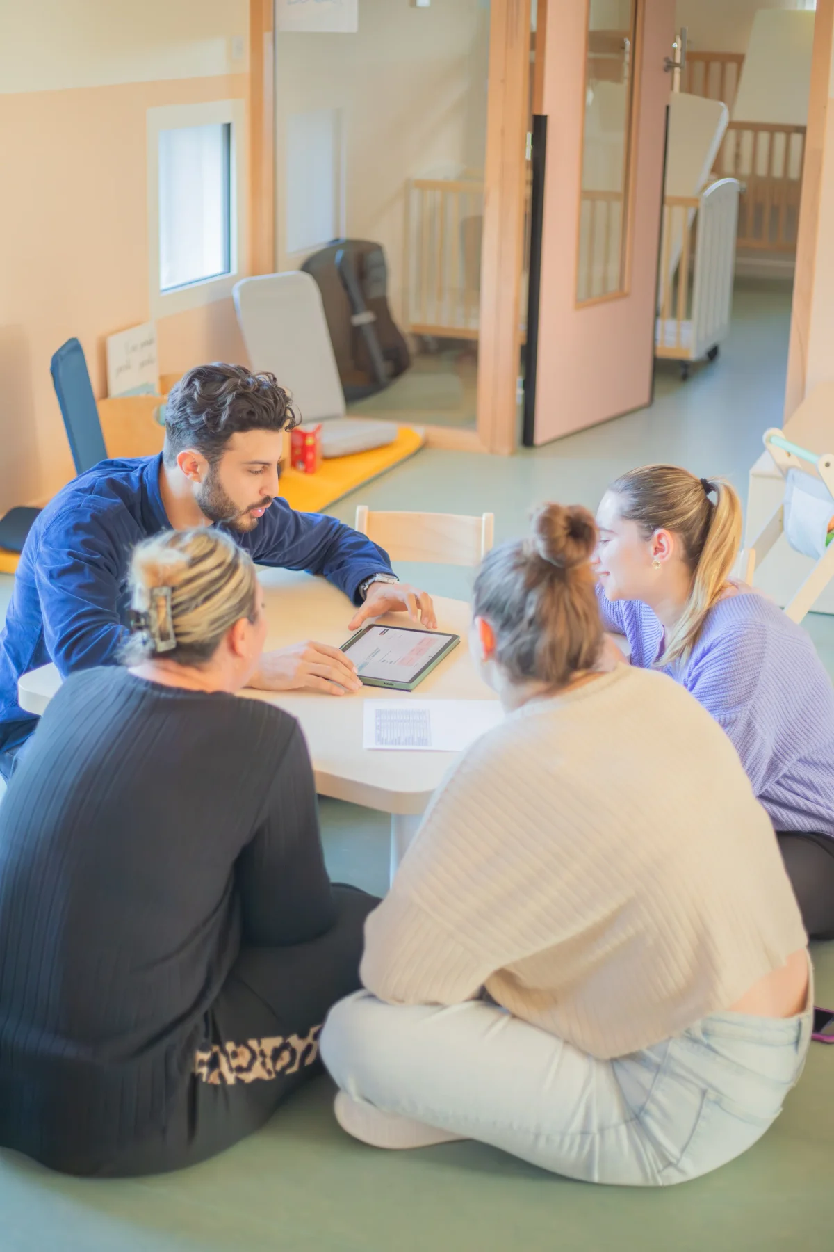 Romain montrant Leia sur tablette à l'équipe, assis par terre dans une crèche