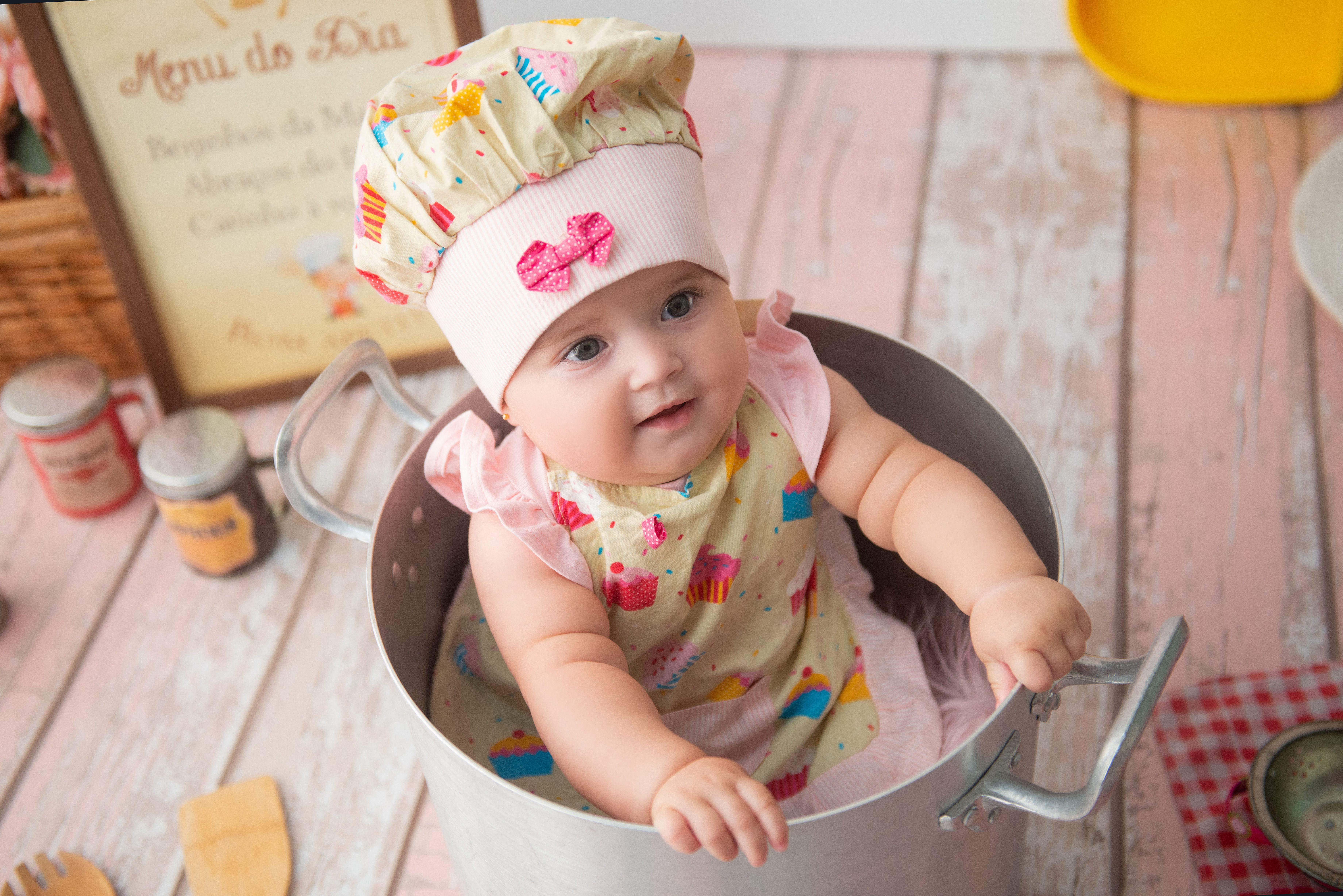 Bébé portant une toque et un tablier de cuisinier, entouré d'ustensiles de cuisine