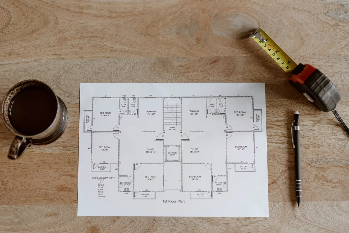 Plan de locaux vu de dessus avec un mètre ruban, un crayon et une tasse de café sur une table en bois