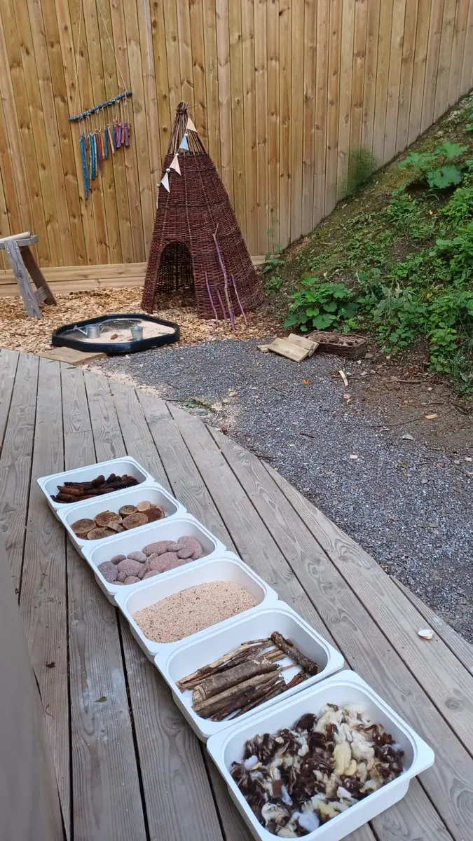 Des bacs de matières naturelles alignés sur une terrasse, un tipi en osier derrière
