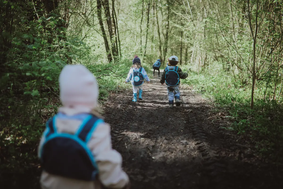 Trois jeunes enfants avec des sacs à dos marchent sur un chemin forestier